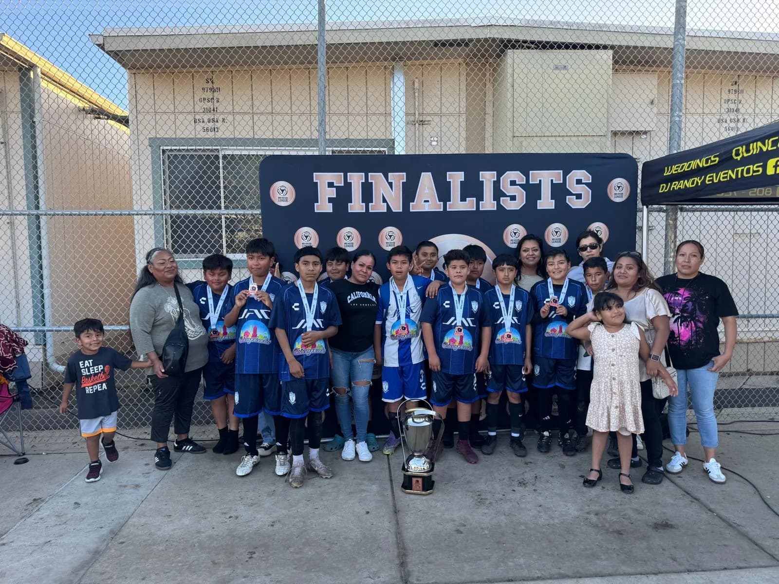 A local youth soccer team sponsored by Chilangolandia, wearing blue jerseys with the Chilangolandia logo, holding medals beside a finalists banner and trophy.